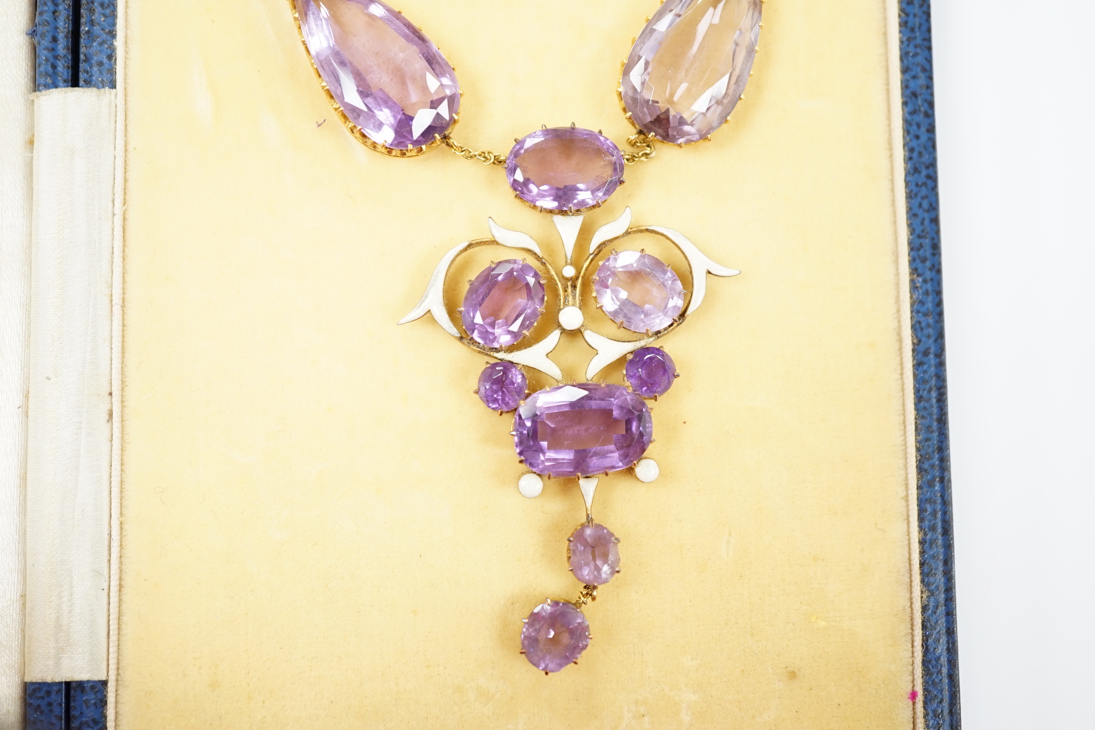 An early 20th century yellow metal, amethyst and enamel set suite of jewellery, comprising a drop necklace, 56cm and a par of matching drop earrings, 33mm, gross weight 38.1 grams.